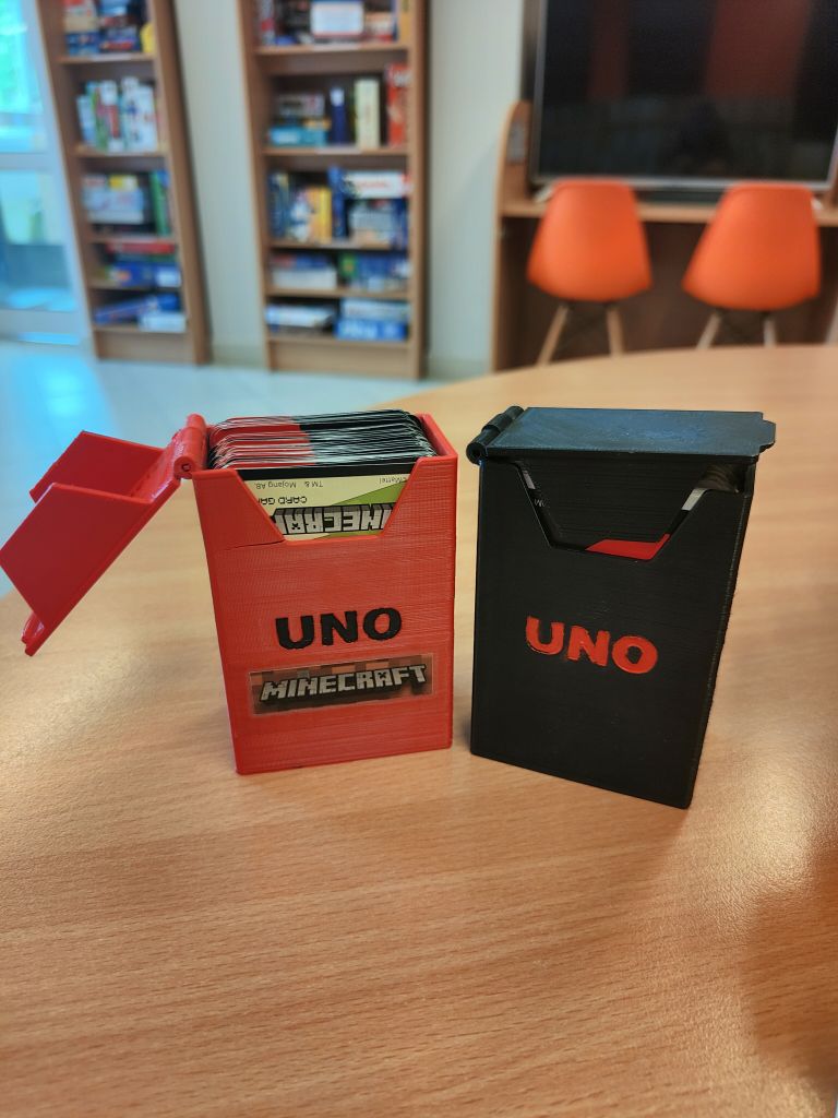 Czerwone pudełko z czarnym napisem UNO i naklejką z napisem Minecraft z kartami w środku, obok czarne pudełko z czerwonym napisem UNO z kartami w środku