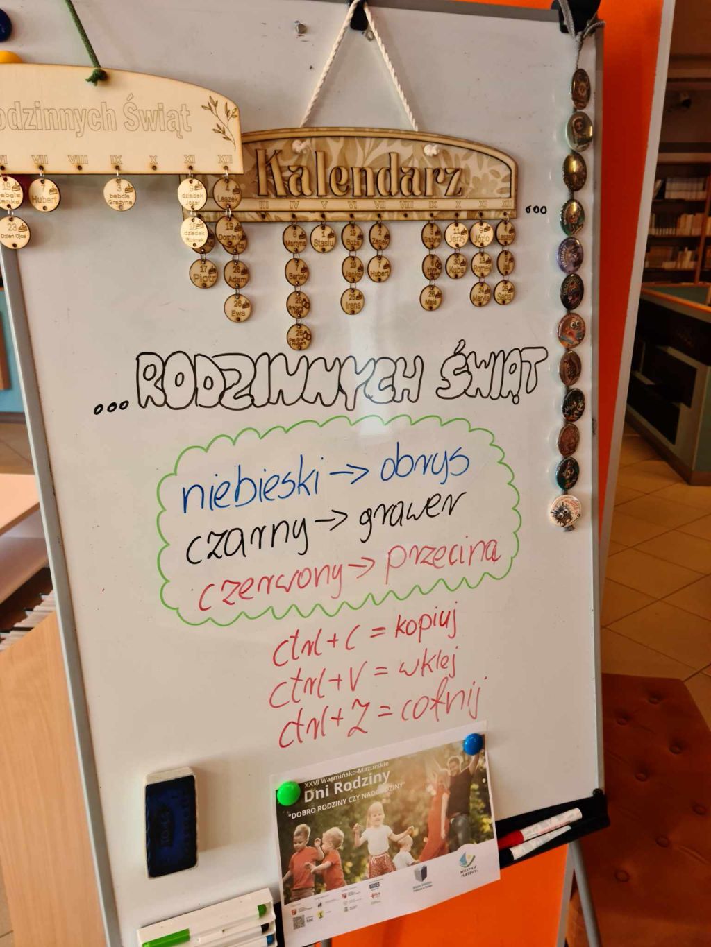 Biała tablica, na której wisi kalendarz ze sklejki, pod nim kolorowe napisy