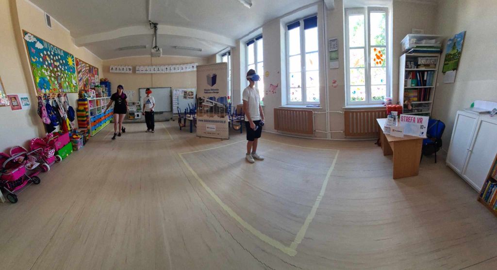Zdjęcie panoramiczne, sala przedszkolna, dwie osoby grają goglami VR