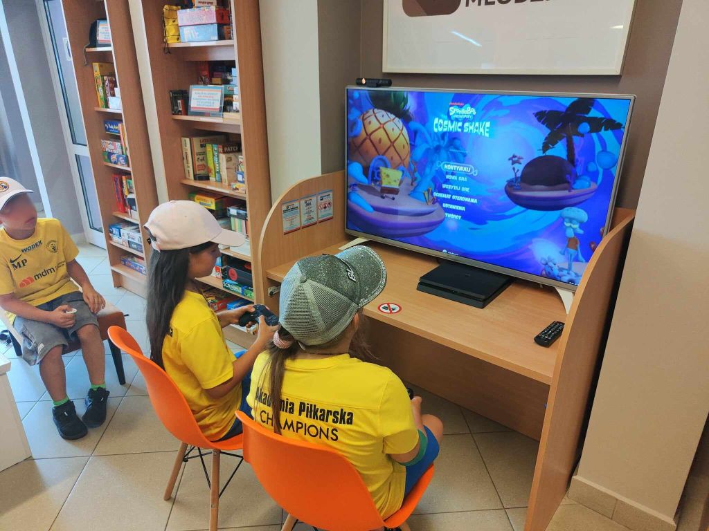 dwie dziewczynki grają na konsoli, przed nimi telewizor