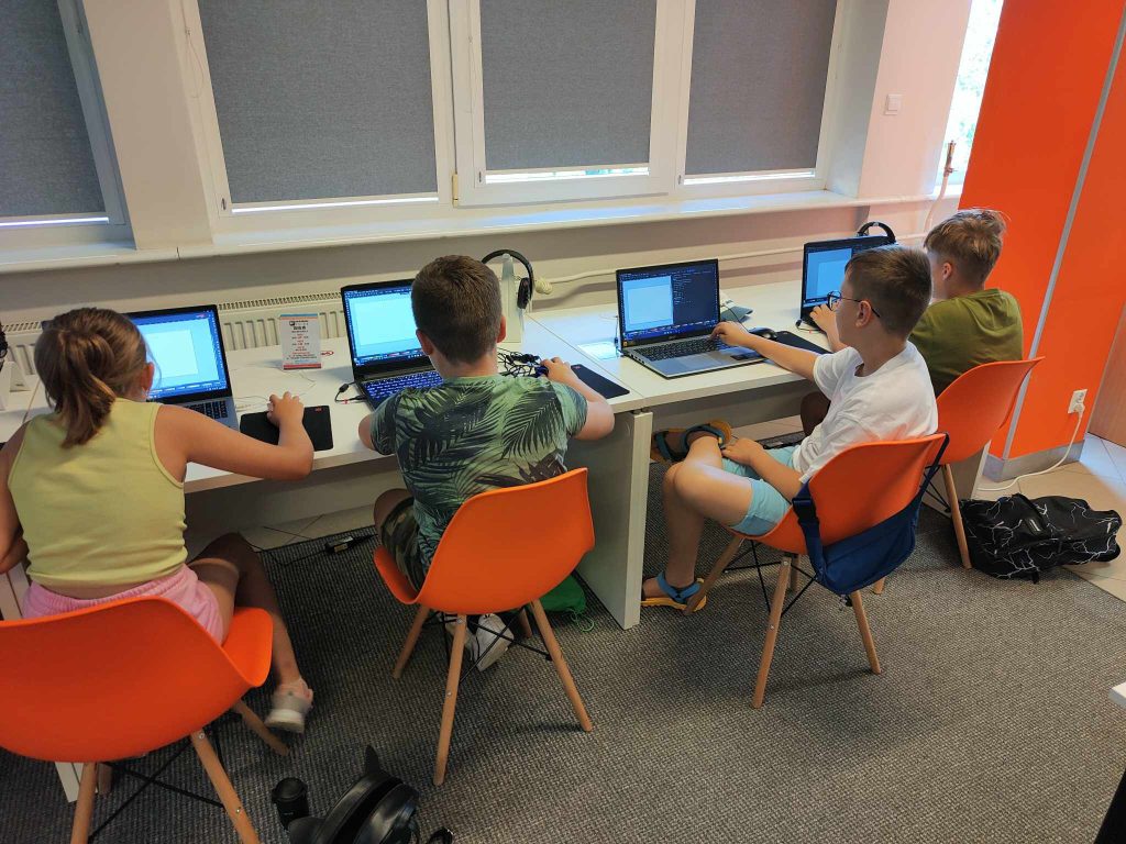 czworo dzieci siedzi przed laptopami