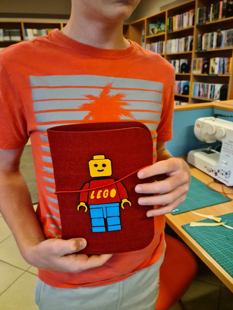 Chłopiec prezentuje filcowy segregator z filcową aplikacją ludzika lego