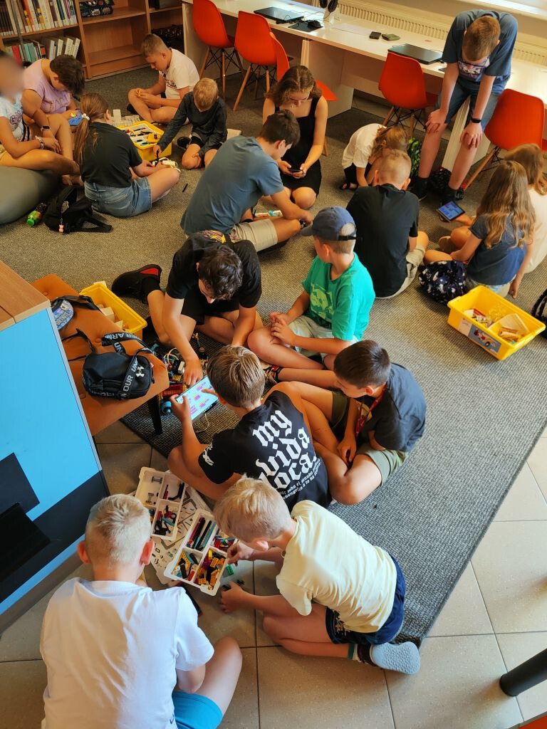 Grupa dzieci siedzi na wykładzinie układając elementy klocków lego