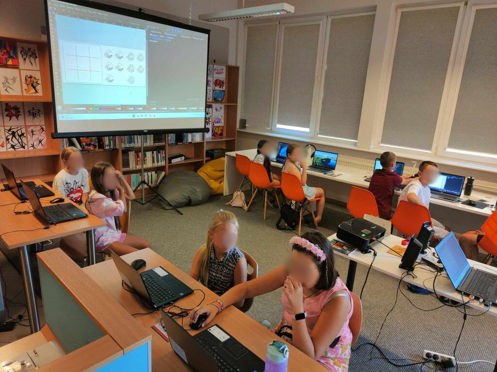 grupa dzieci siedzi przy laptopach