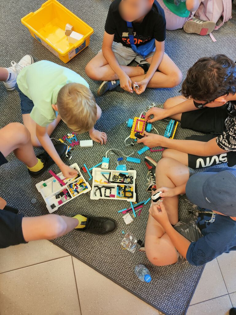Grupa dzieci siedzi na wykładzinie układając elementy klocków lego