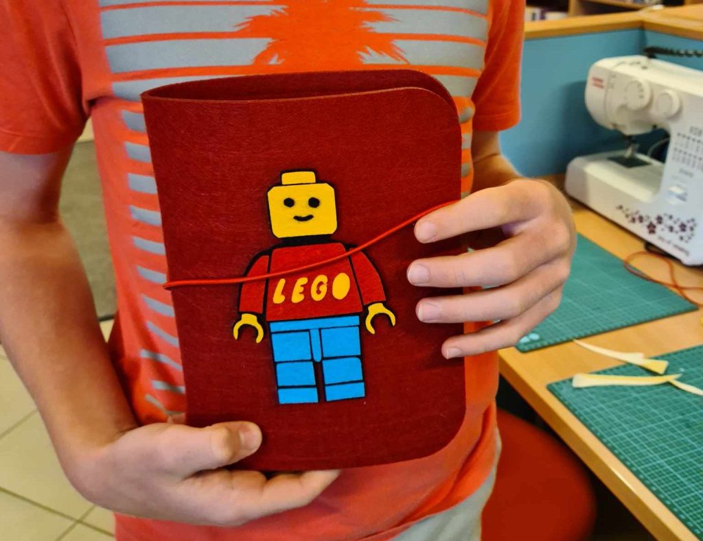Chłopiec prezentuje filcowy segregator z filcową aplikacją ludzika lego