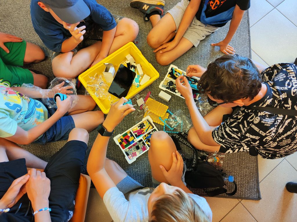 Grupa dzieci siedzi na wykładzinie układając elementy klocków lego