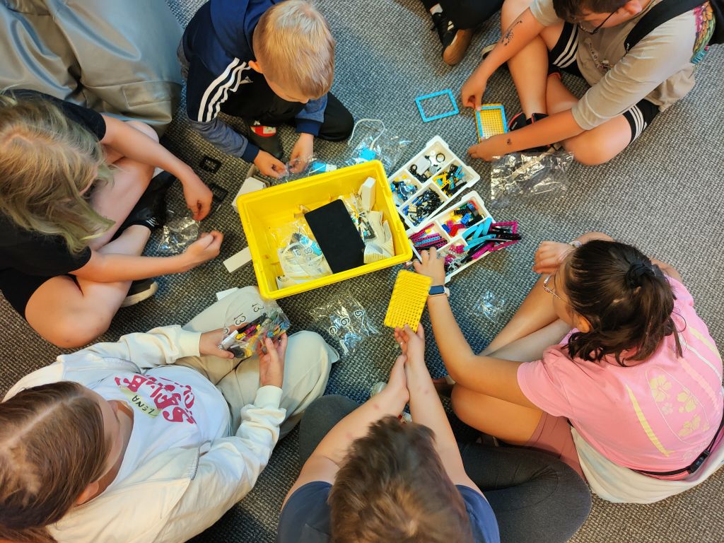 Grupa dzieci siedzi na wykładzinie układając elementy klocków lego