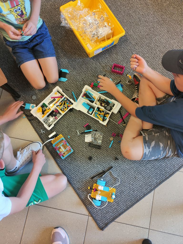 Grupa dzieci siedzi na wykładzinie układając elementy klocków lego