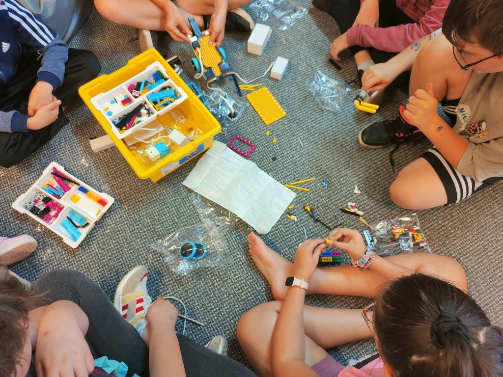 Grupa dzieci siedzi na wykładzinie układając elementy klocków lego
