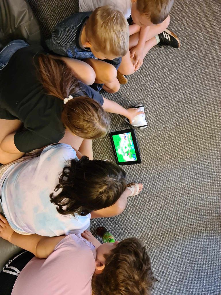 Dzieci siedzą w grupie na wykładzinie, przed nimi stoi tablet i robot Photon