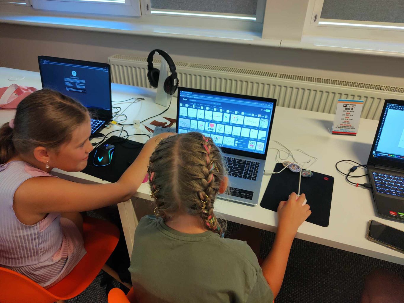 dwie dziewczynki siedzą przed laptopami