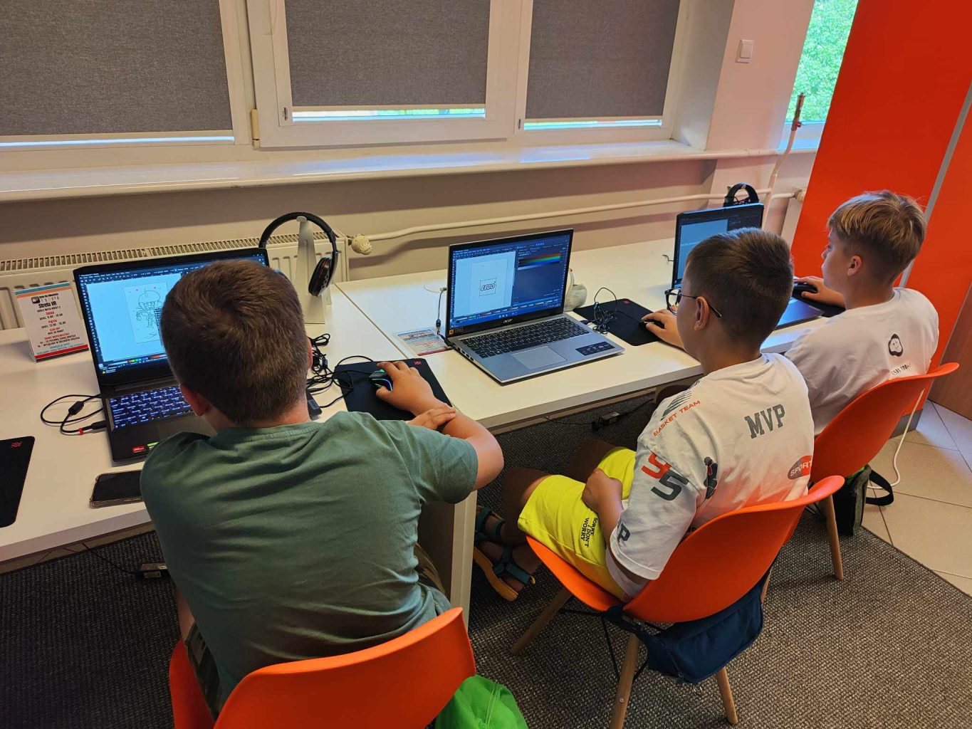 trzech chłopców siedzi przed laptopami