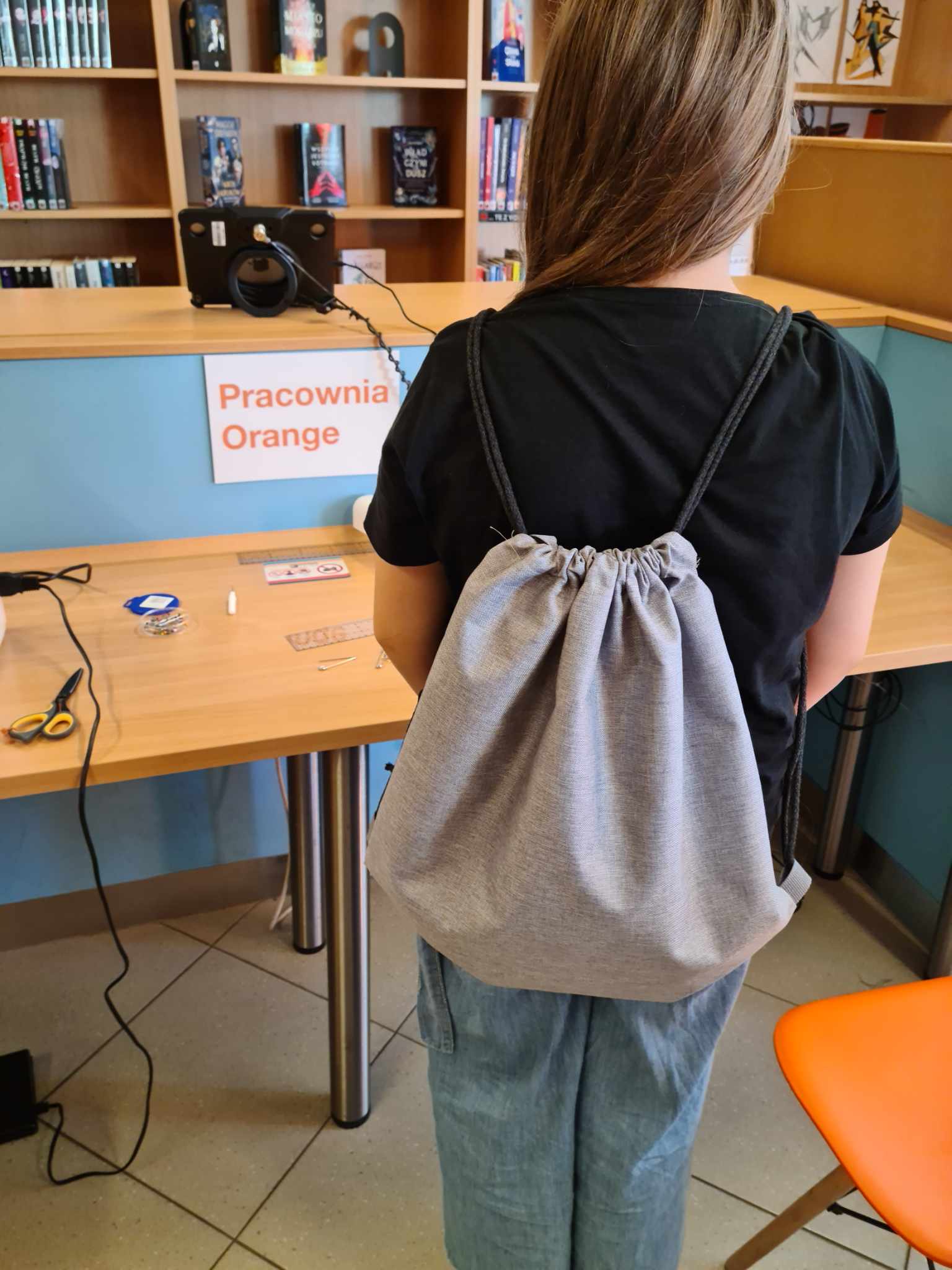 Dziewczyna stoi tyłem, na plecach ma założony workoplecak