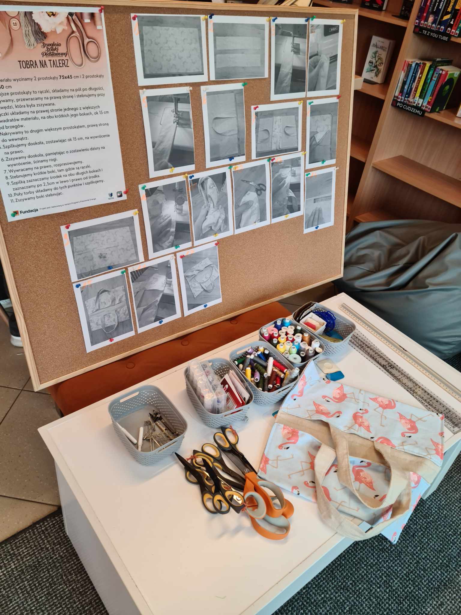 tablica korkowa z przypiętymi czarnobiałymi zdjęciami, pod nią przybory krawieckie na stoliku