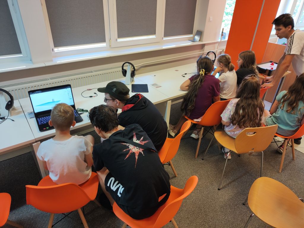 Grupa dzieci siedzi przy biurkach i korzysta z laptopów