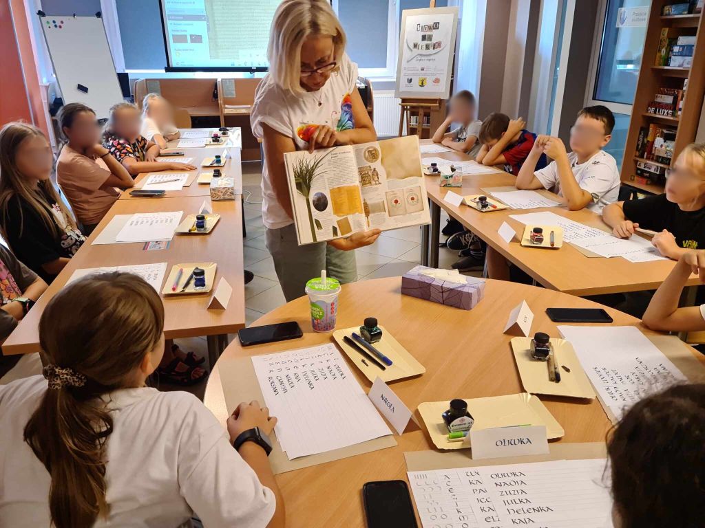 Kobieta stoi na przeciwko dzieci i pokazuje im ilustracje w książce