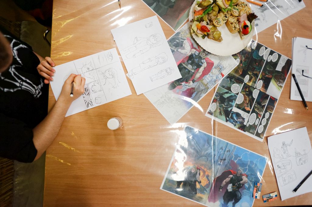 ujęcie na stół z komiksami i ręce rysujące komiks