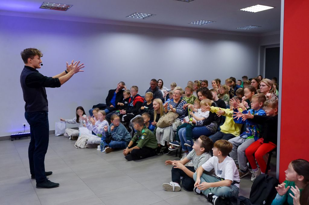 mężczyzna stoi i wyciąga ręce przed siebie, przed nim widownia robi to samo