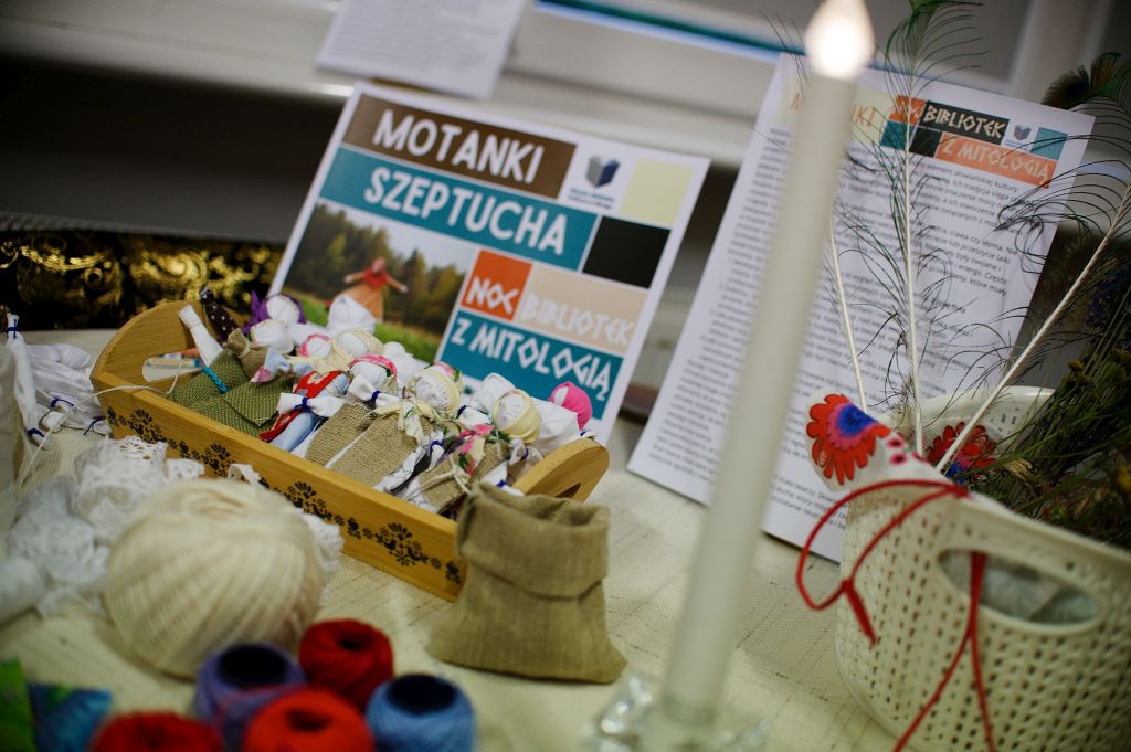 na stole leży drewniana taca, w niej kilka laleczek motanek, za nimi kartka z napisem Motanki Szeptucha, wokół przybory krawieckie