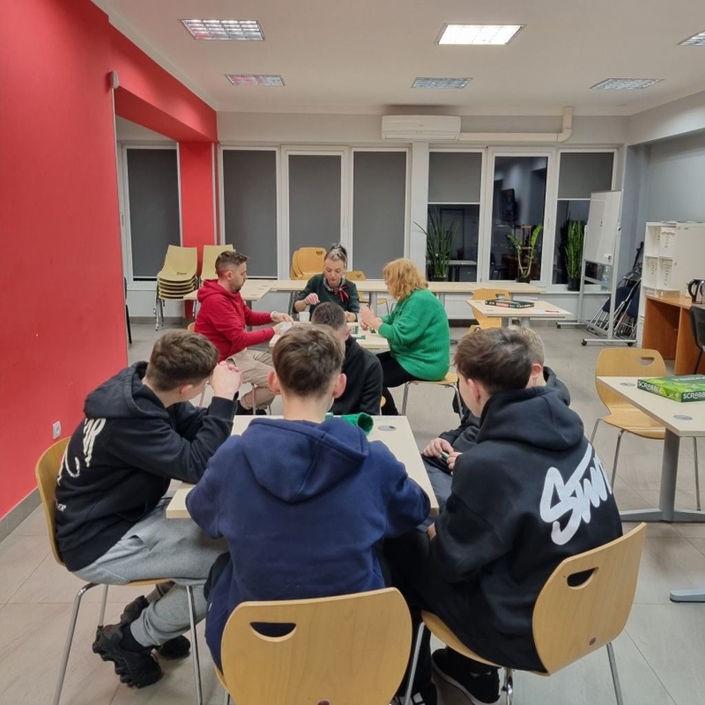 grupa osób siedzi przy stołach i gra w Scrabble
