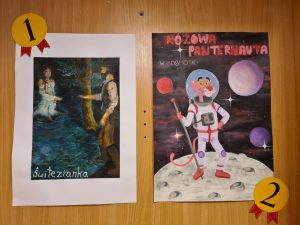 Zbliżenie na dwie nagrodzone ilustracje na tle drewnianej półki. Po lewej „Świtezianka” z parą nad wodą, po prawej „Różowa Panternauta w kosmosie” z Różową Panterą w skafandrze astronauty. Na ilustracjach oznaczenia miejsc: pierwsze i drugie.