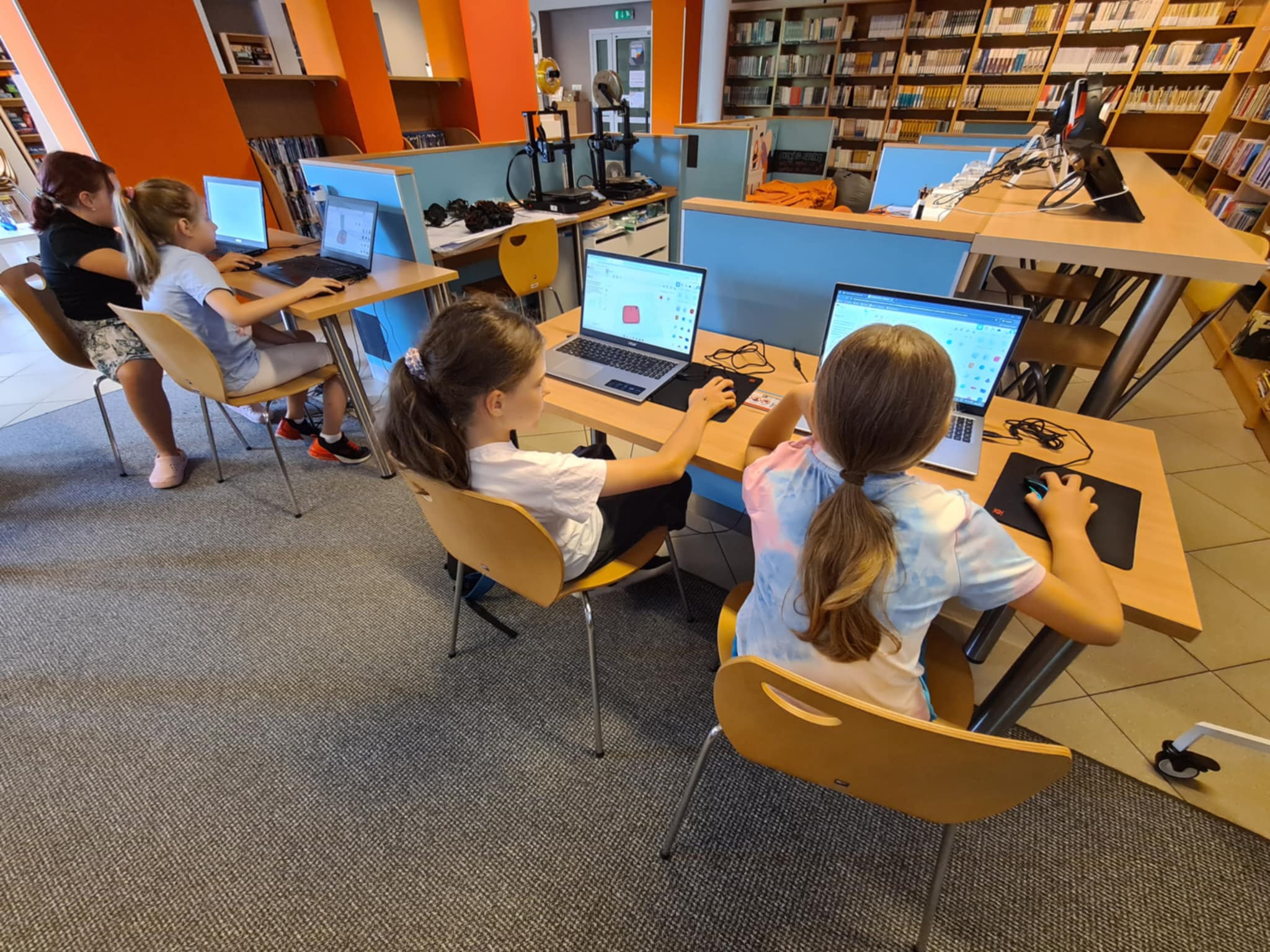 Cztery dziewczynki siedzą przy laptopach i projektują modele 3D w bibliotece