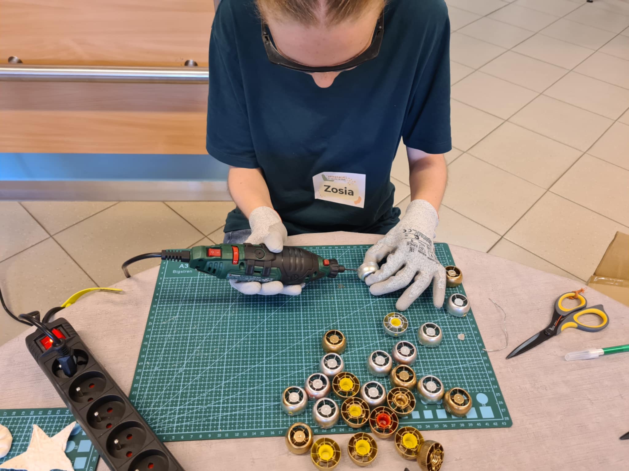 Dziewczynka pracuje w rękawicach z wiertarką, przygotowuje metalowe części do dekoracji.