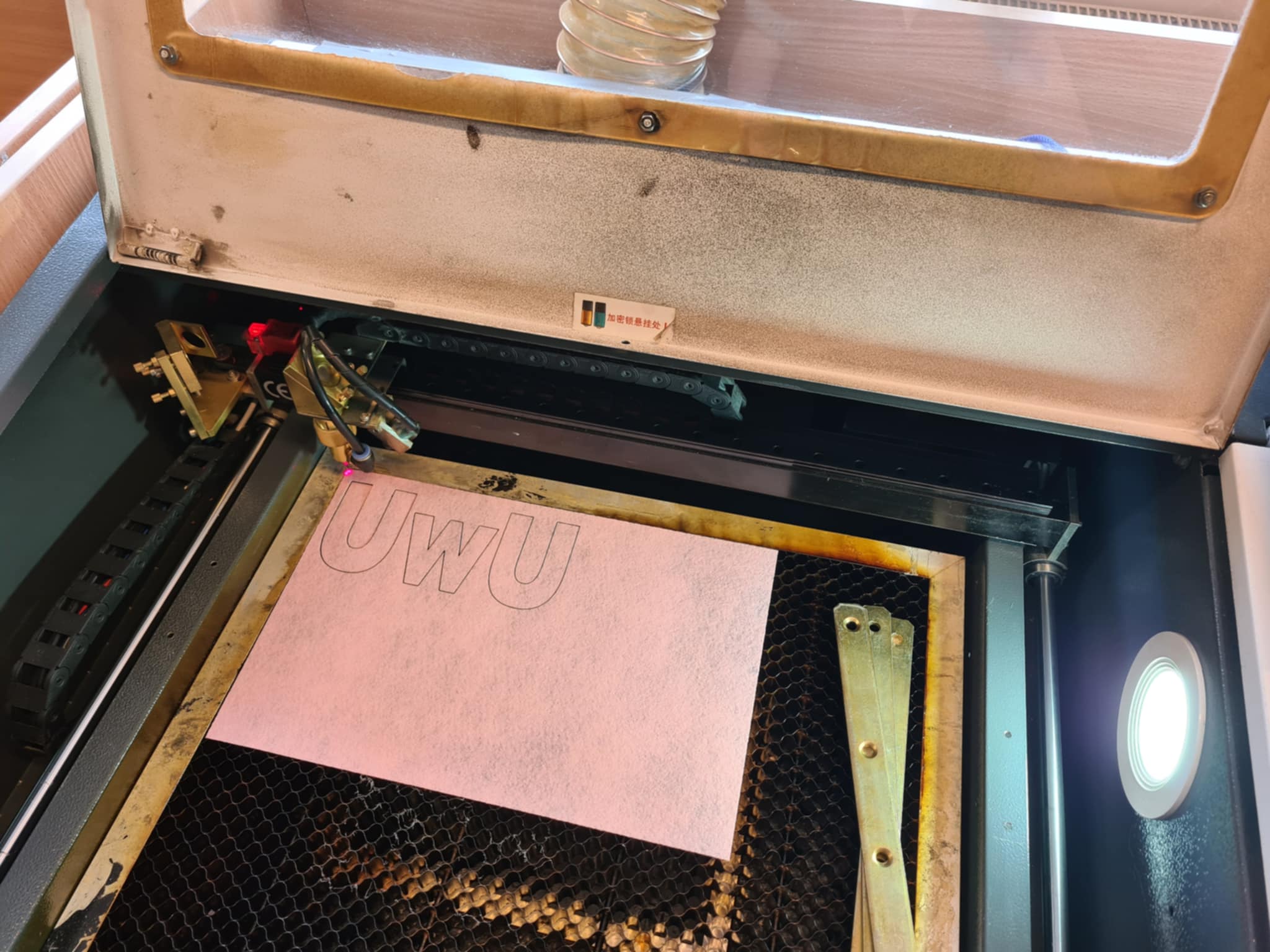 Laser wycina napis „UWU” w arkuszu materiału.