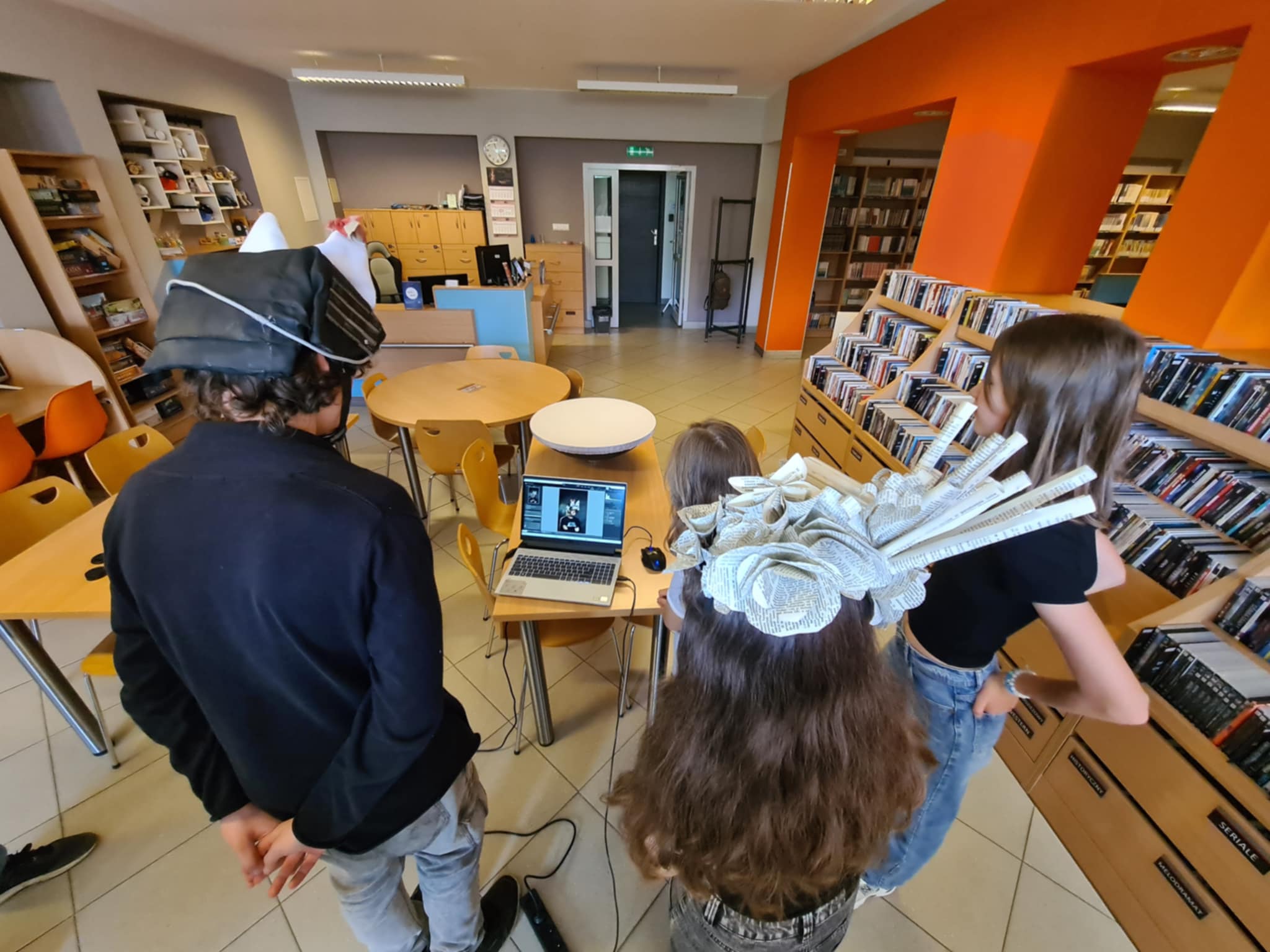 Uczestnicy warsztatów w bibliotece przeglądają zdjęcia na laptopie.