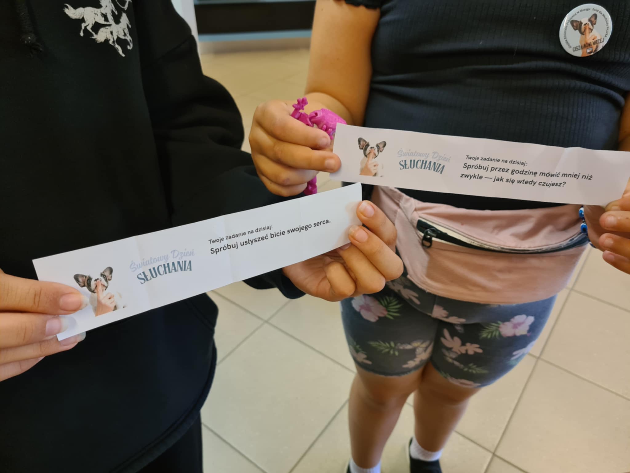 Dwie osoby trzymają karteczki z wylosowanymi zadaniami na Światowy Dzień Słuchania.