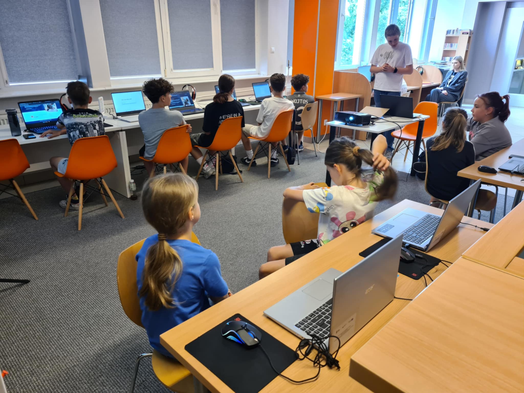 Grupa dzieci i młodzieży pracuje przy komputerach, projektując książki w bibliotece.