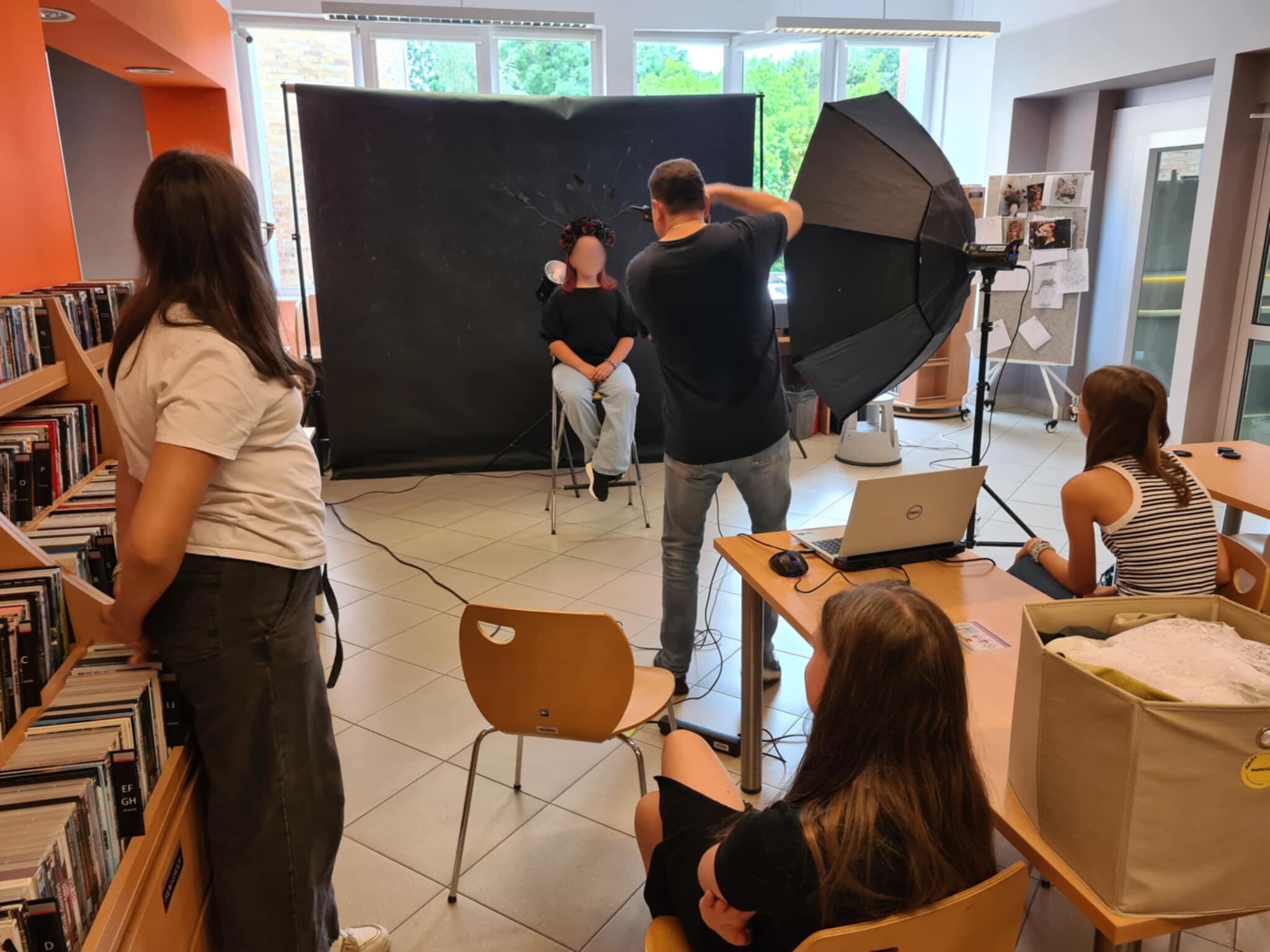 Grupa młodzieży obserwuje fotografa podczas sesji zdjęciowej w bibliotece.