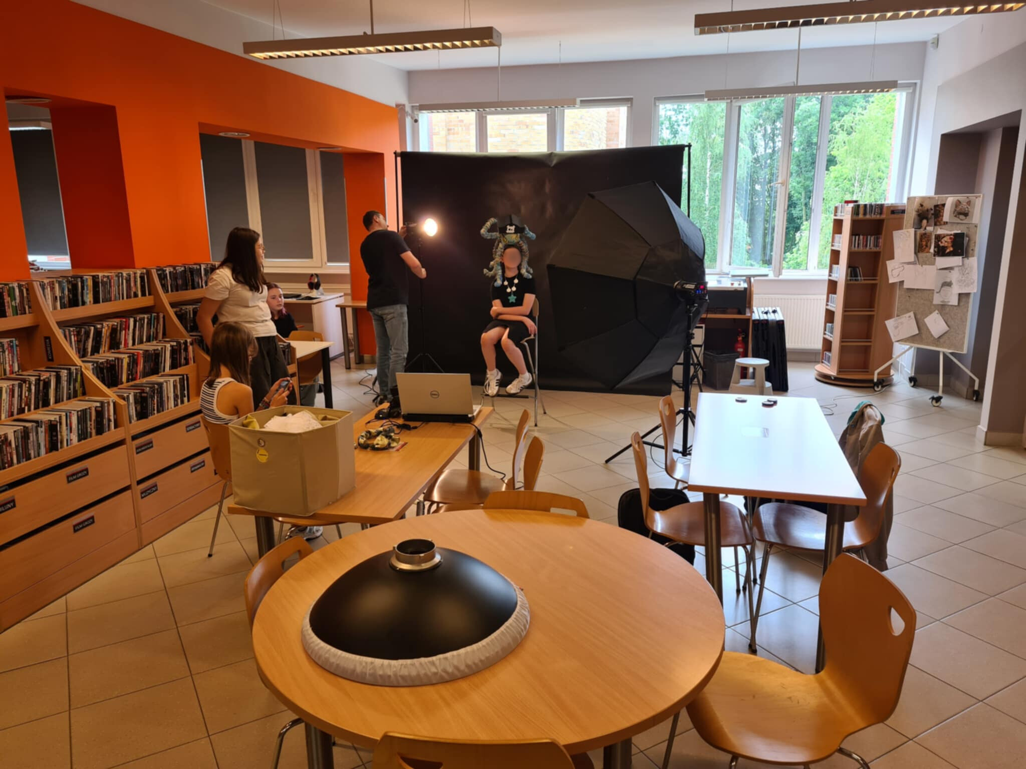 Fotograf i młodzież pracują podczas sesji zdjęciowej w bibliotece, model siedzi na tle czarnego ekranu.