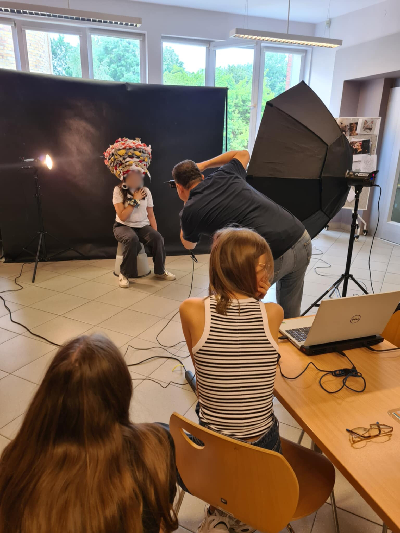Fotograf robi zdjęcia modelce w kolorowym nakryciu głowy, inni uczestnicy obserwują.