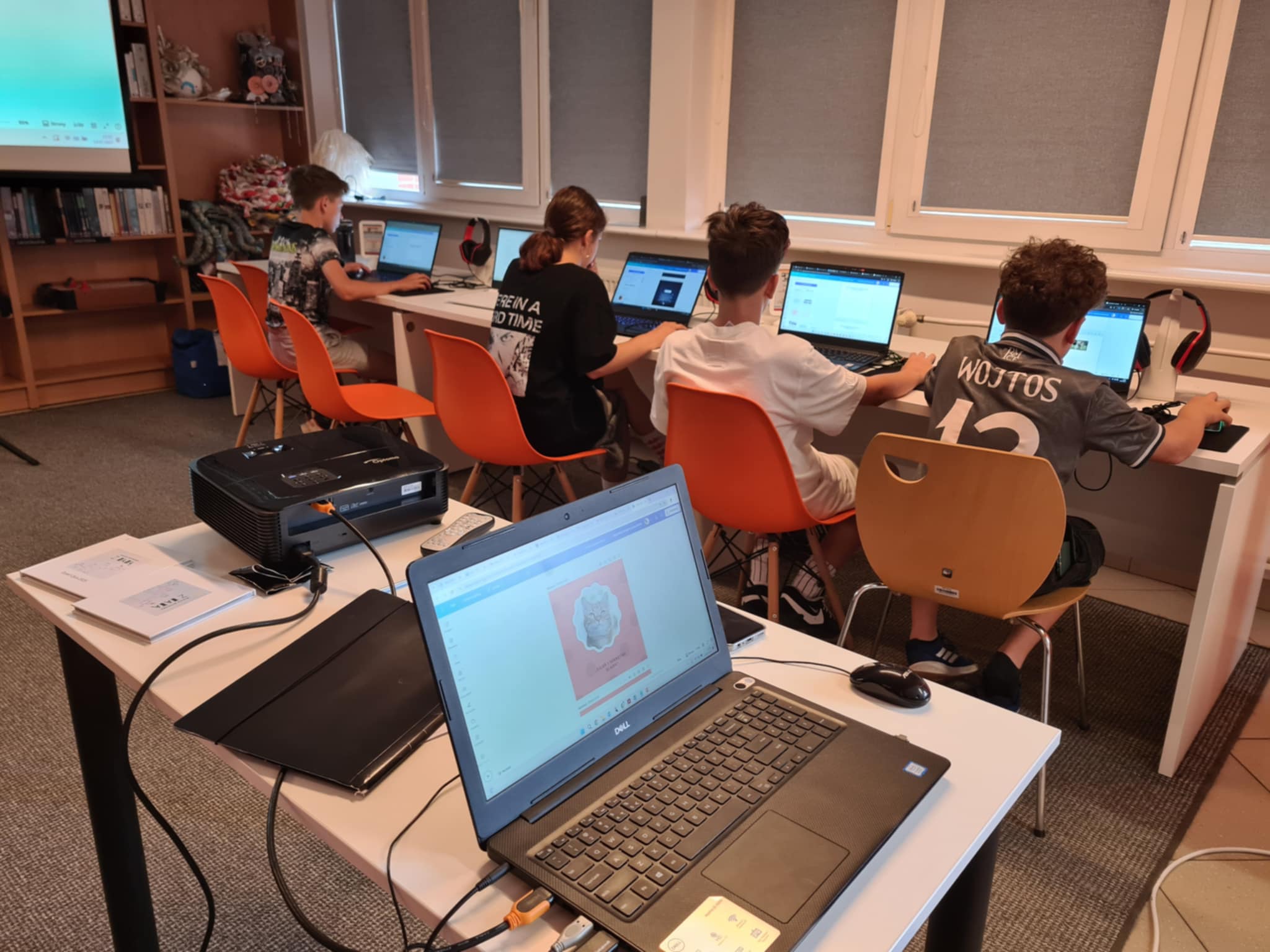 Młodzież skupiona na pracy przy komputerach, projektując własne książki w nowoczesnej sali biblioteki.