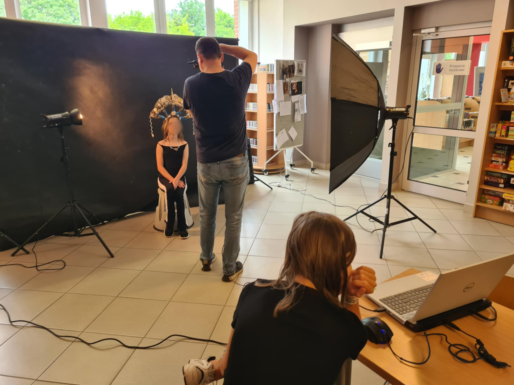 Fotograf robi zdjęcie dziewczynie w kreatywnej koronie w bibliotecznym studiu.