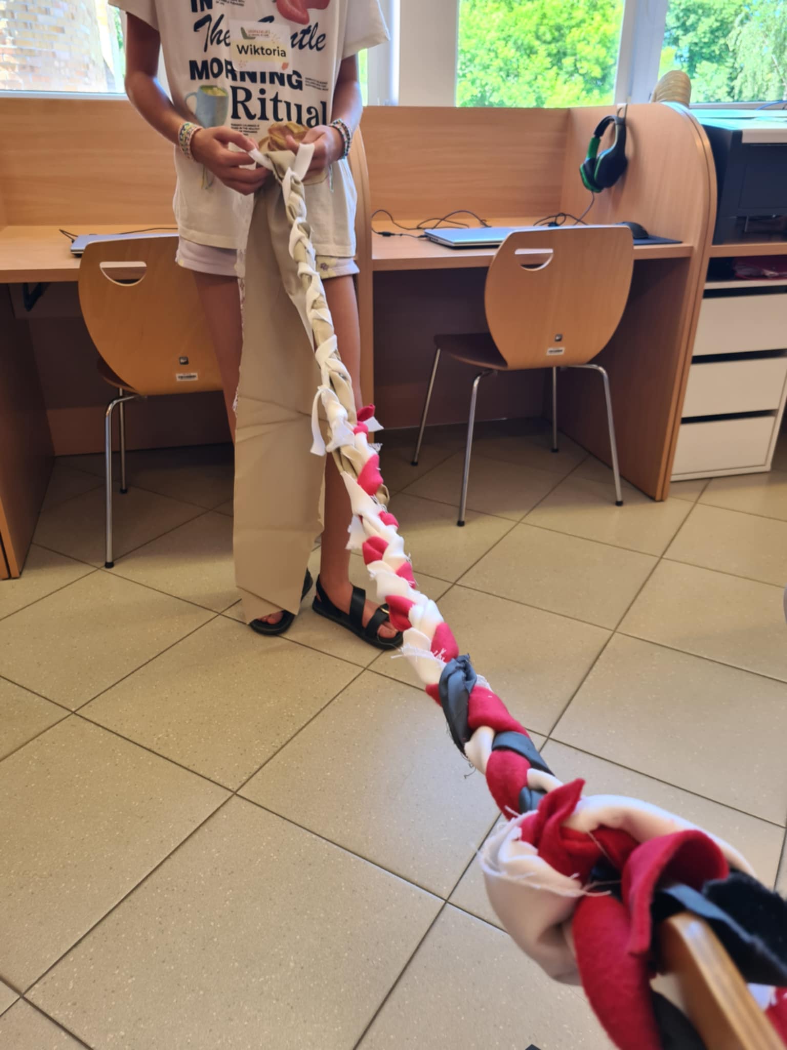 Dziewczynka zaplata długi kolorowy warkocz z materiału.