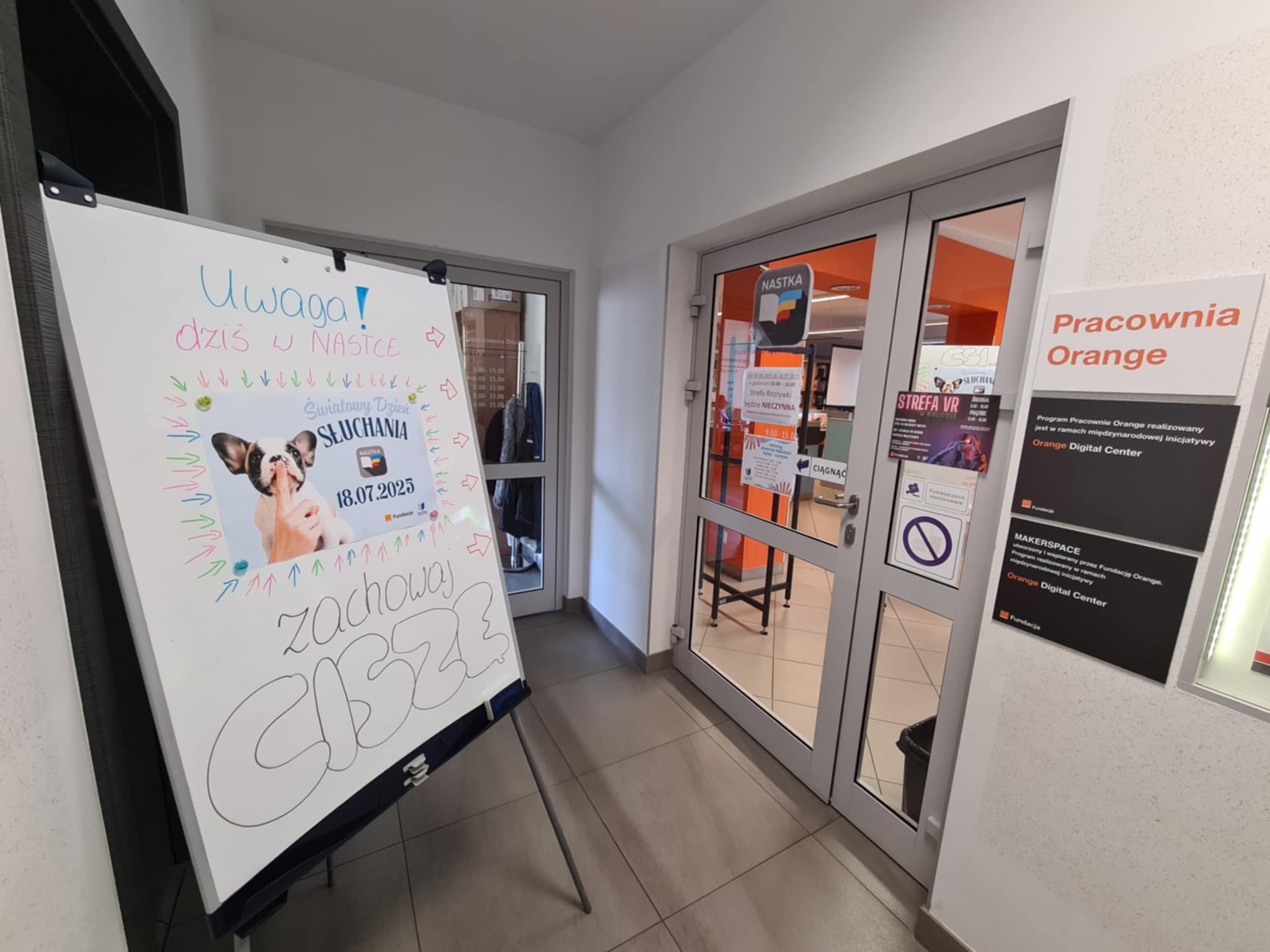 Plansza z informacją o Światowym Dniu Słuchania ustawiona przy wejściu do Pracowni Orange.