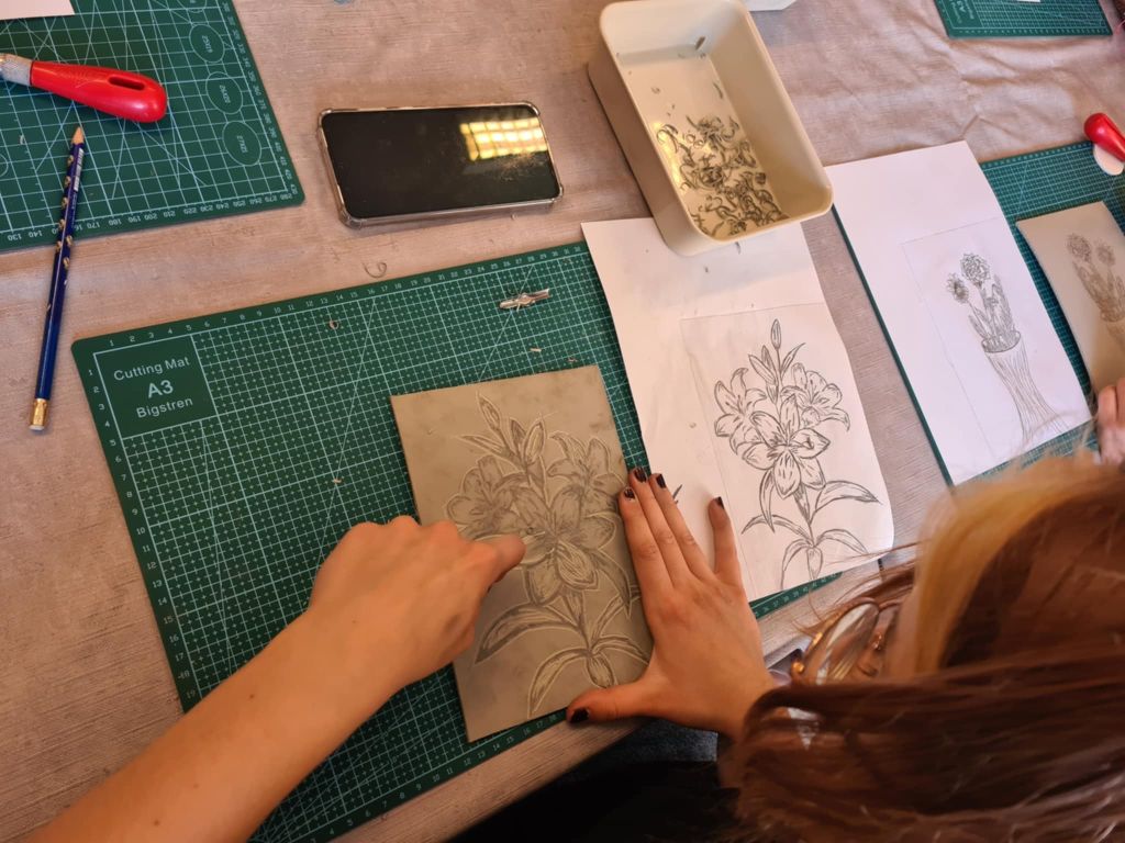 Ręce uczestnika ryjącego wzór kwiatów w linoleum przy pomocy dłuta.