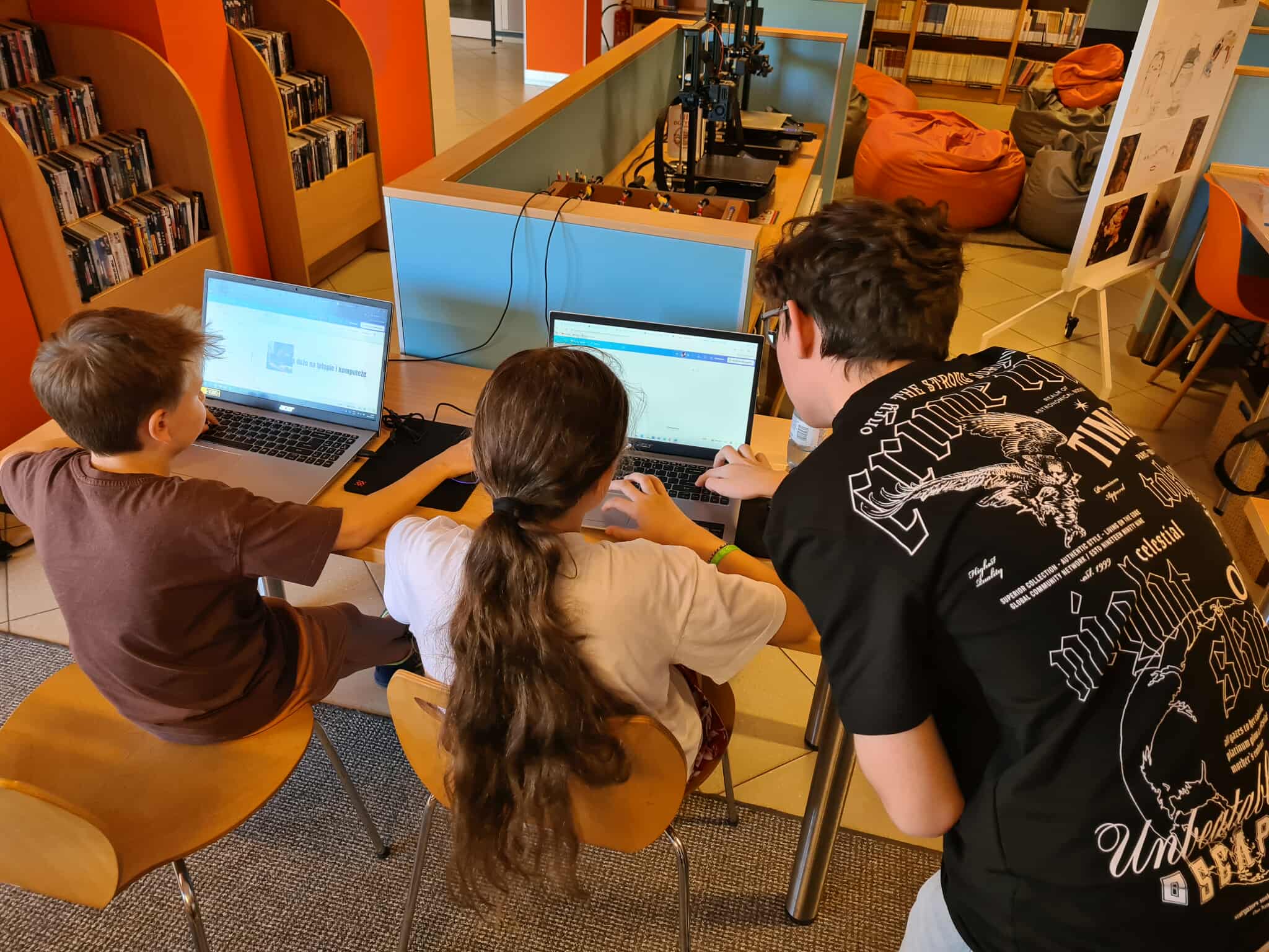 Trójka dzieci pracuje na laptopach w bibliotece, projektując w programie graficznym.