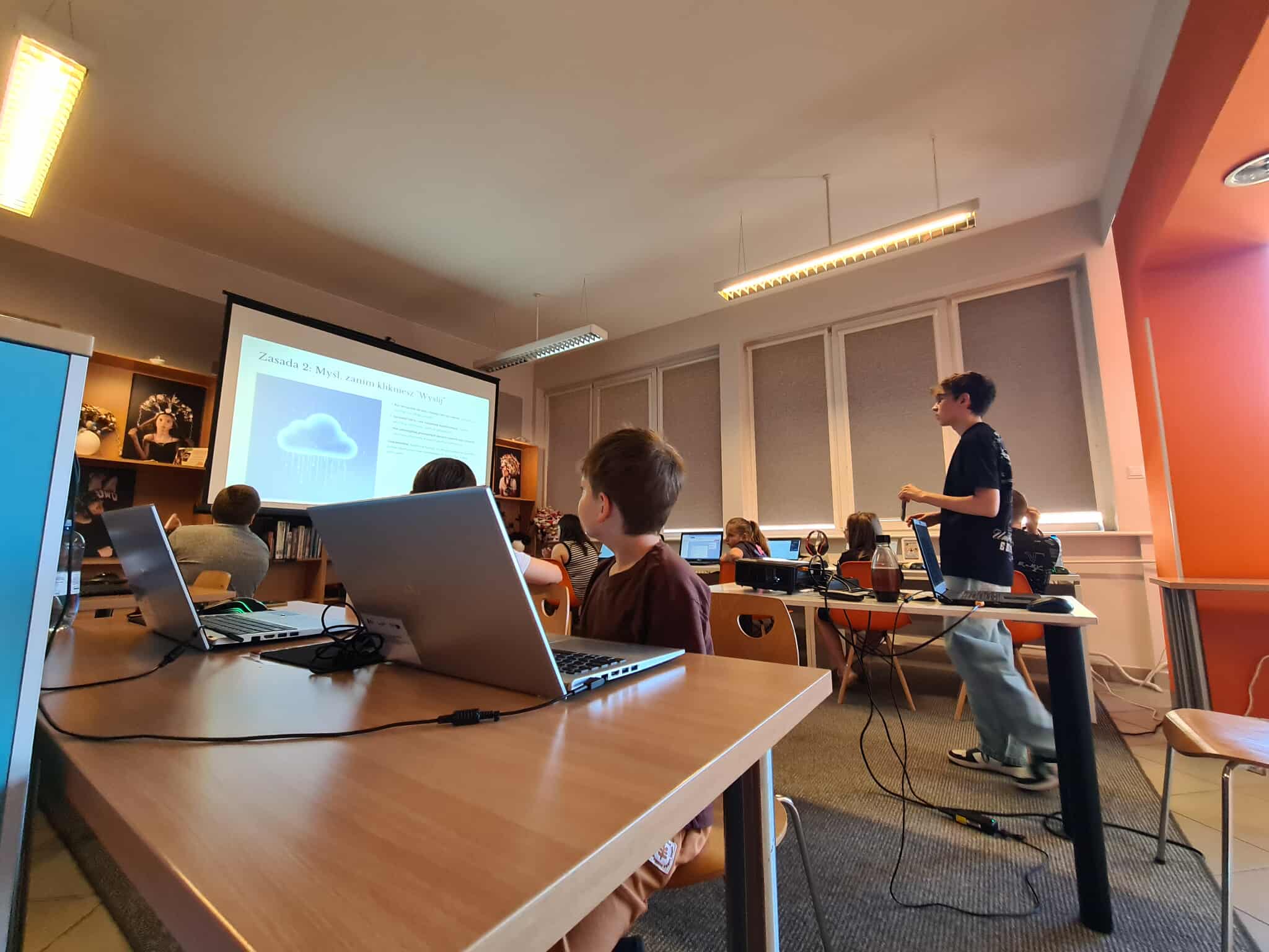Młodzież ogląda prezentację o bezpieczeństwie w internecie w sali komputerowej biblioteki.