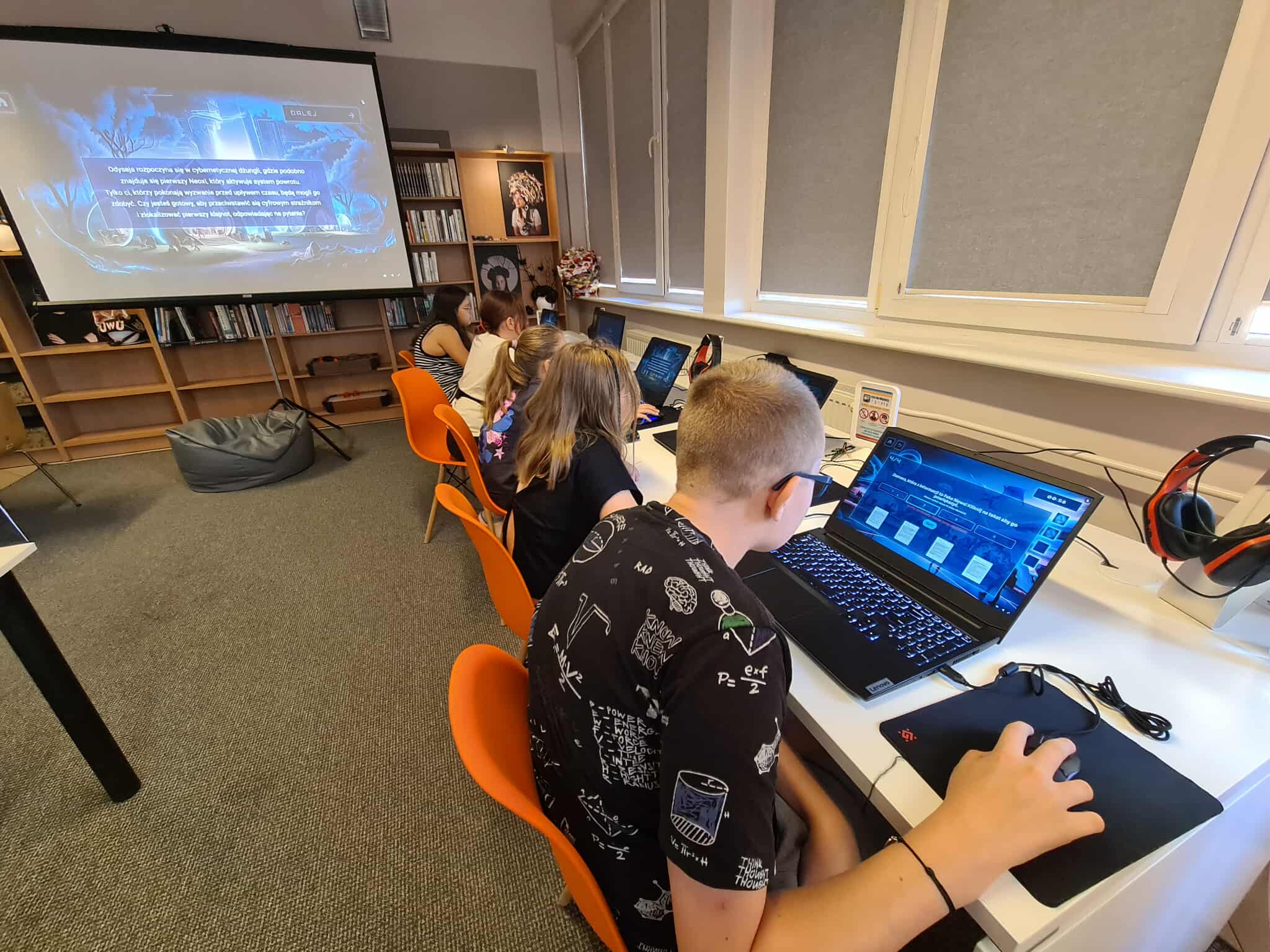 Uczestnicy zajęć komputerowych grają w edukacyjną grę na laptopach.