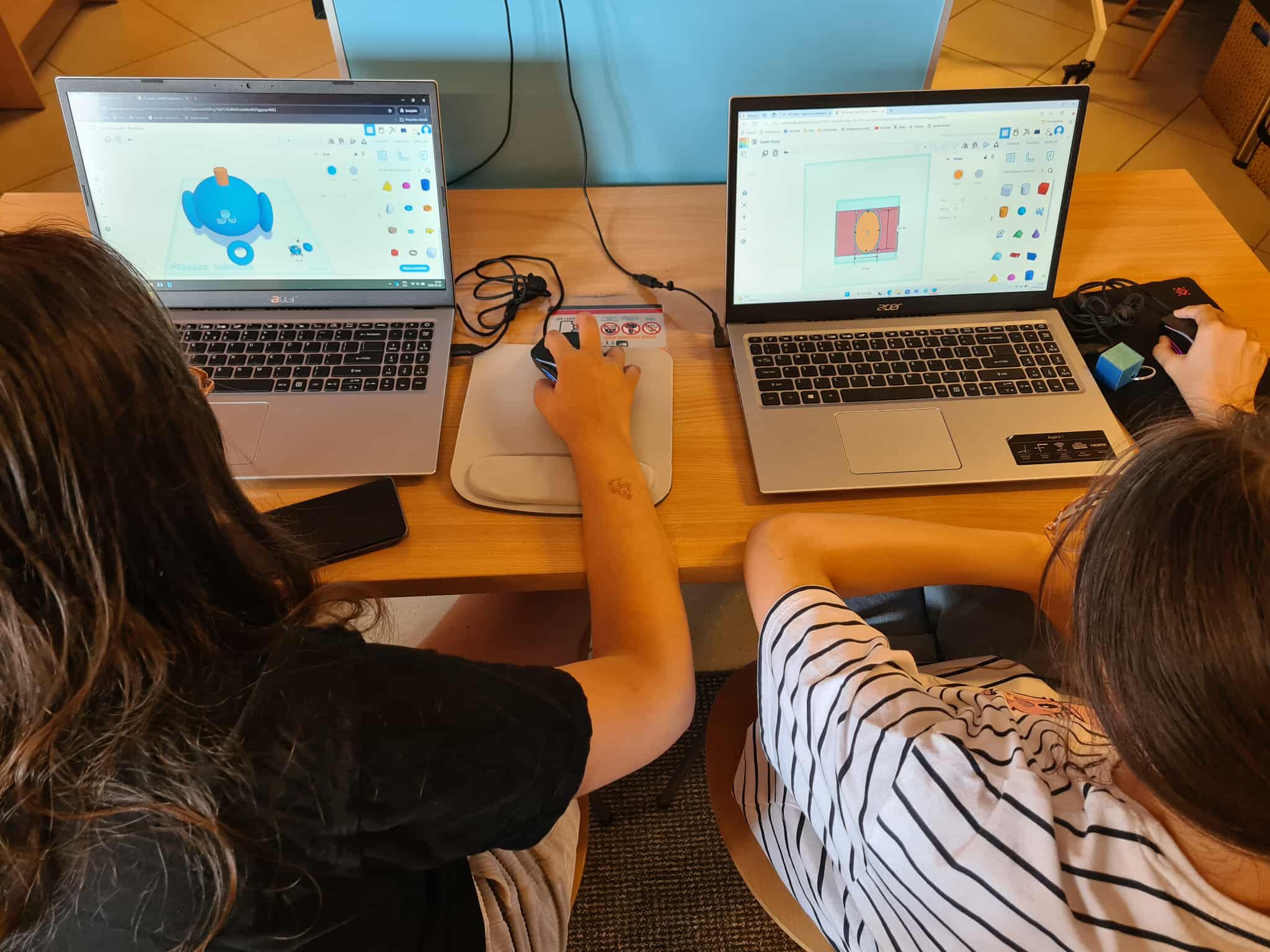 Projektowanie 3D na laptopach – dwie dziewczynki przy laptopach Acer tworzą własne modele 3D w programie Tinkercad, na ekranach widać figurki i kształty.