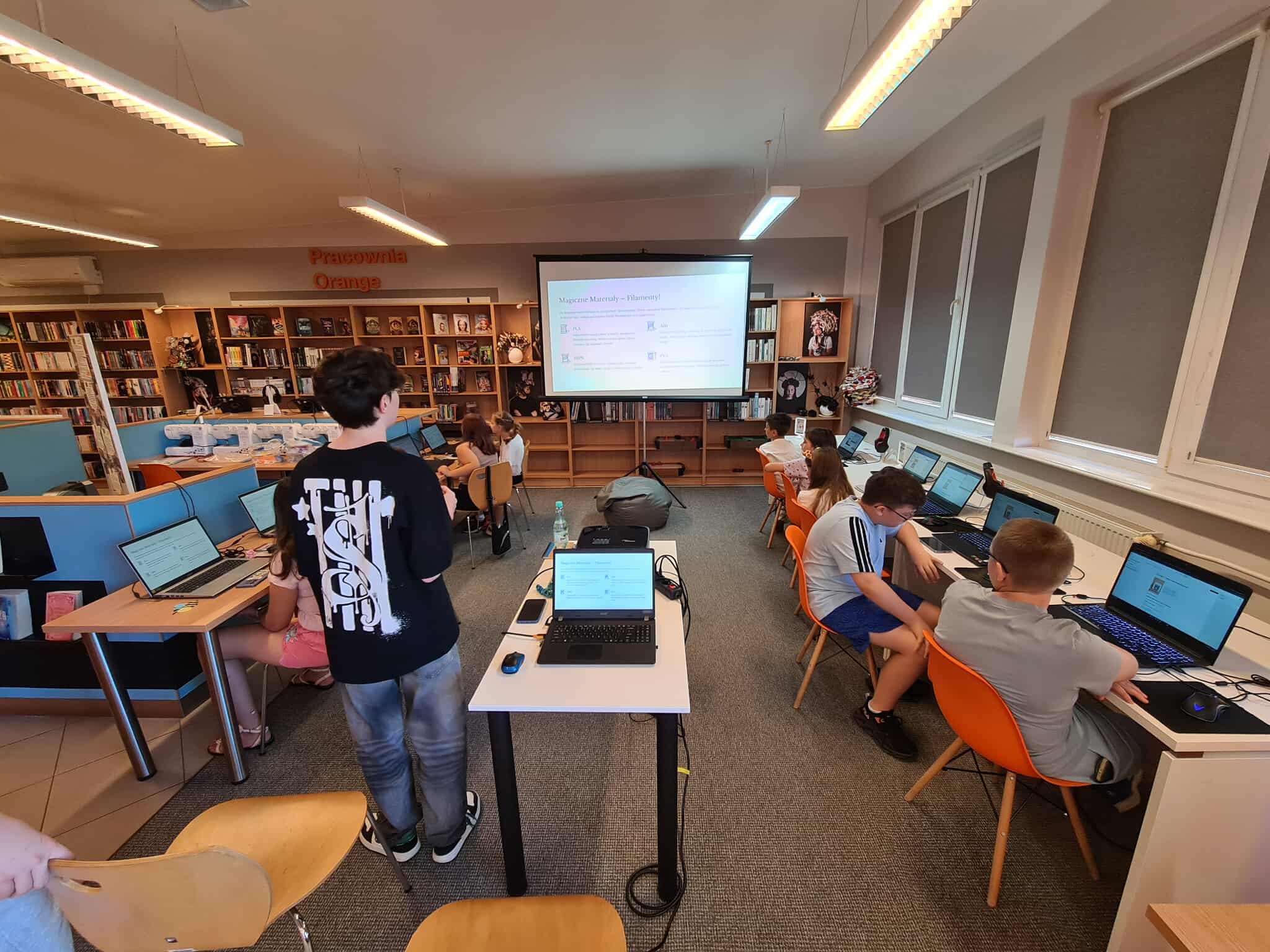 Sala warsztatowa w bibliotece – dzieci pracują przy laptopach podczas zajęć z modelowania 3D.
