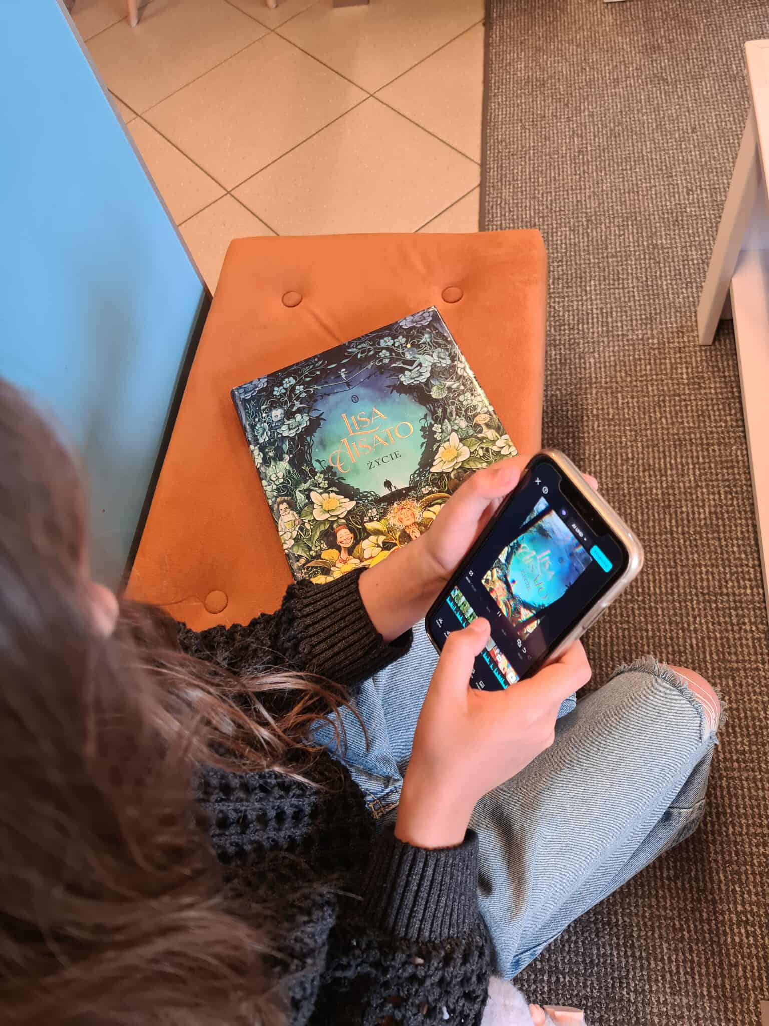 Dziewczyna edytuje zdjęcie książki „Życie” Lisy Aisato na ekranie telefonu.
