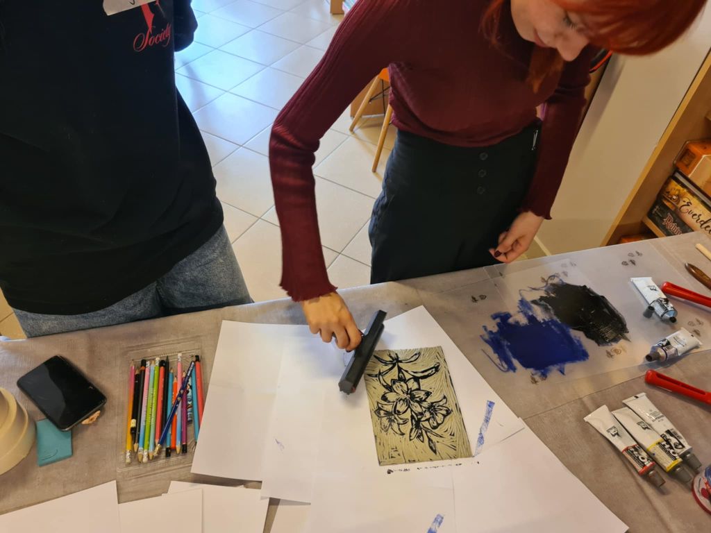 Instruktorka wałkuje farbę drukarską na płytce linorytu z motywem kwiatów.
