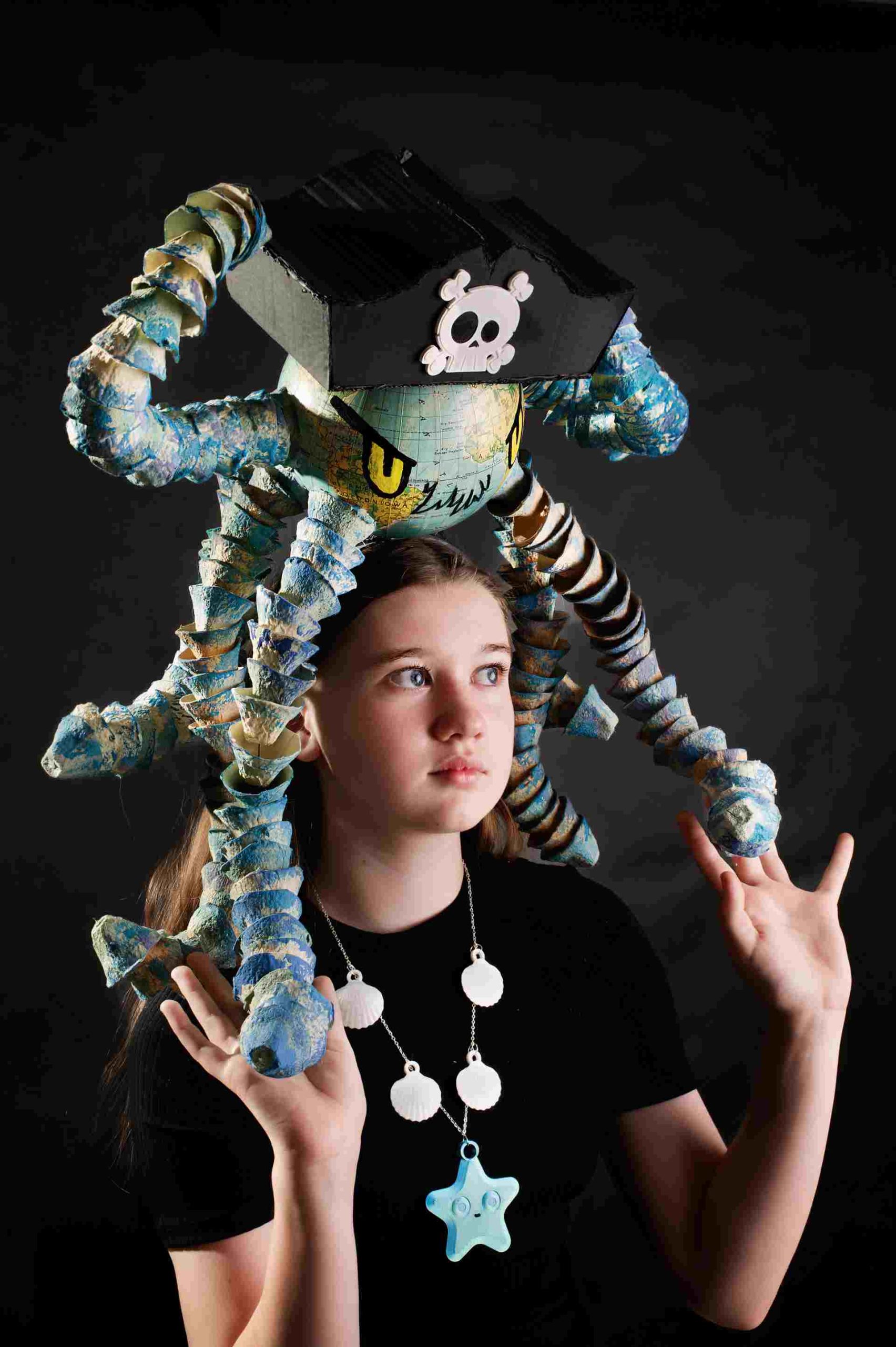 Dziewczynka z kapeluszem przypominającym ośmiornicę z mapy świata, z pirackim motywem, naszyjnik z muszli.