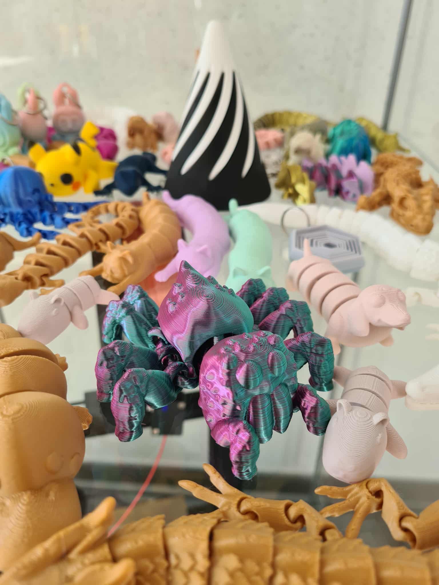 Zbliżenie na kolorowe figurki 3D – w centrum fioletowo-zielony pająk, wokół inne modele zwierząt i postaci.