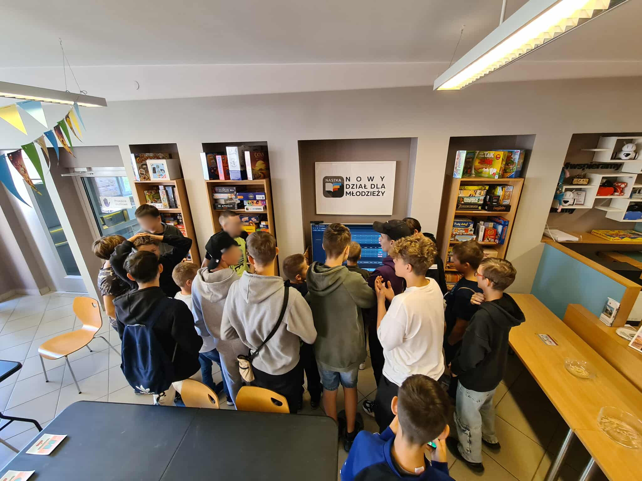 Grupa nastolatków zgromadzona wokół telewizora w dziale NASTKA, śledząca przebieg rozgrywek w turnieju Brawl Stars. Na ścianie widoczny napis „Nowy dział dla młodzieży”.